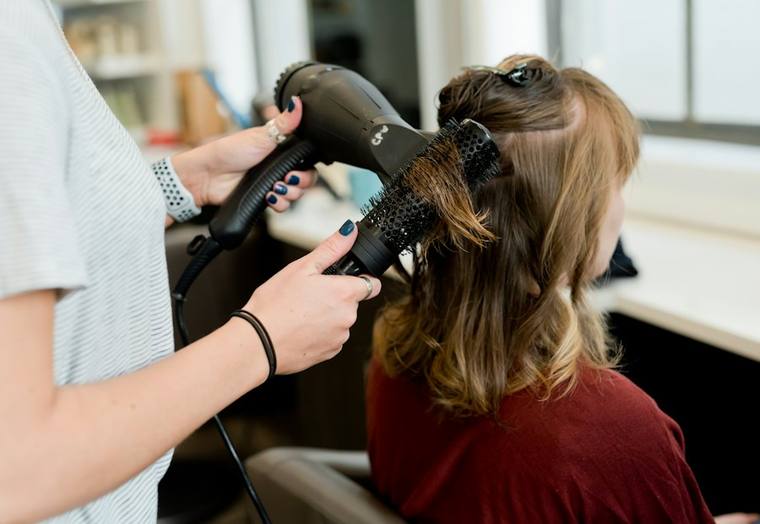 Friseurin föhnt und bürstet die Haare einer Kundin im Salon